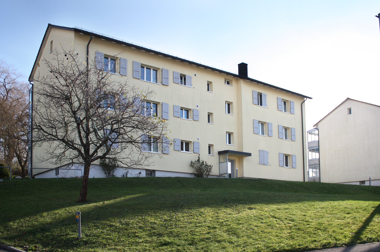 Cremefarbenes Wohnhaus der Siedlung Bischofkänel mit Rasenfläche.