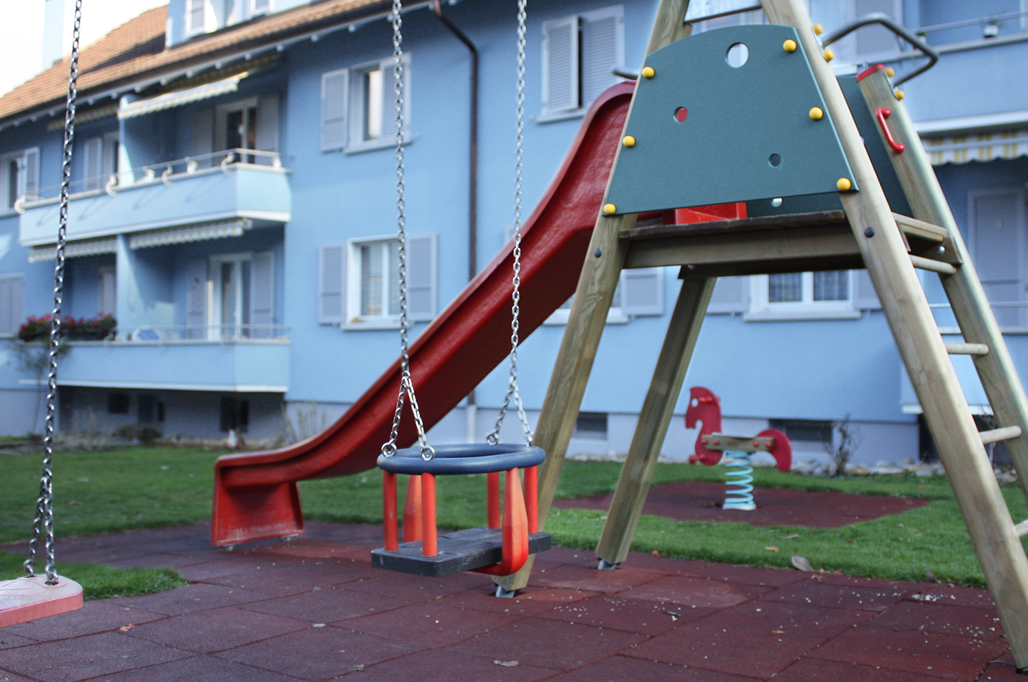 Spielplatz mit Rutsche vor einem blauen Wohnhaus der Siedlung Mettfeld.