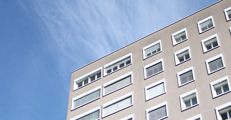 Helles, mehrstöckiges Wohngebäude der Siedlung Mühlefeld vor blauem Himmel.